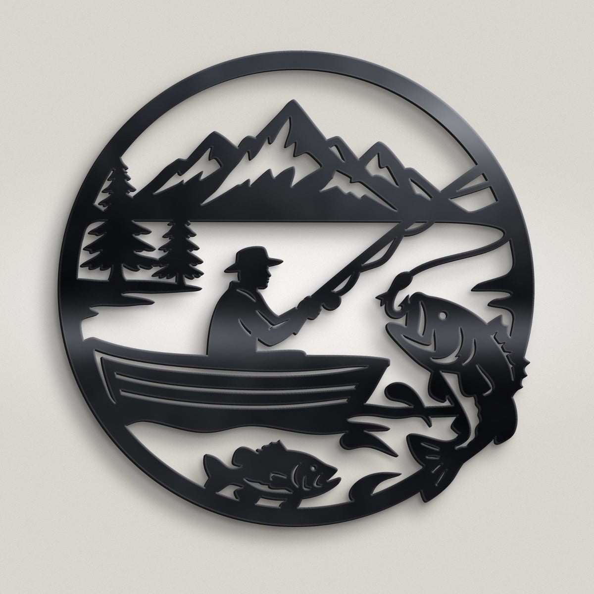 A circular black metal wall art piece featuring a silhouette scene of a fisherman in a boat on a lake with mountains, trees, and fish, shown against a light gray background.
