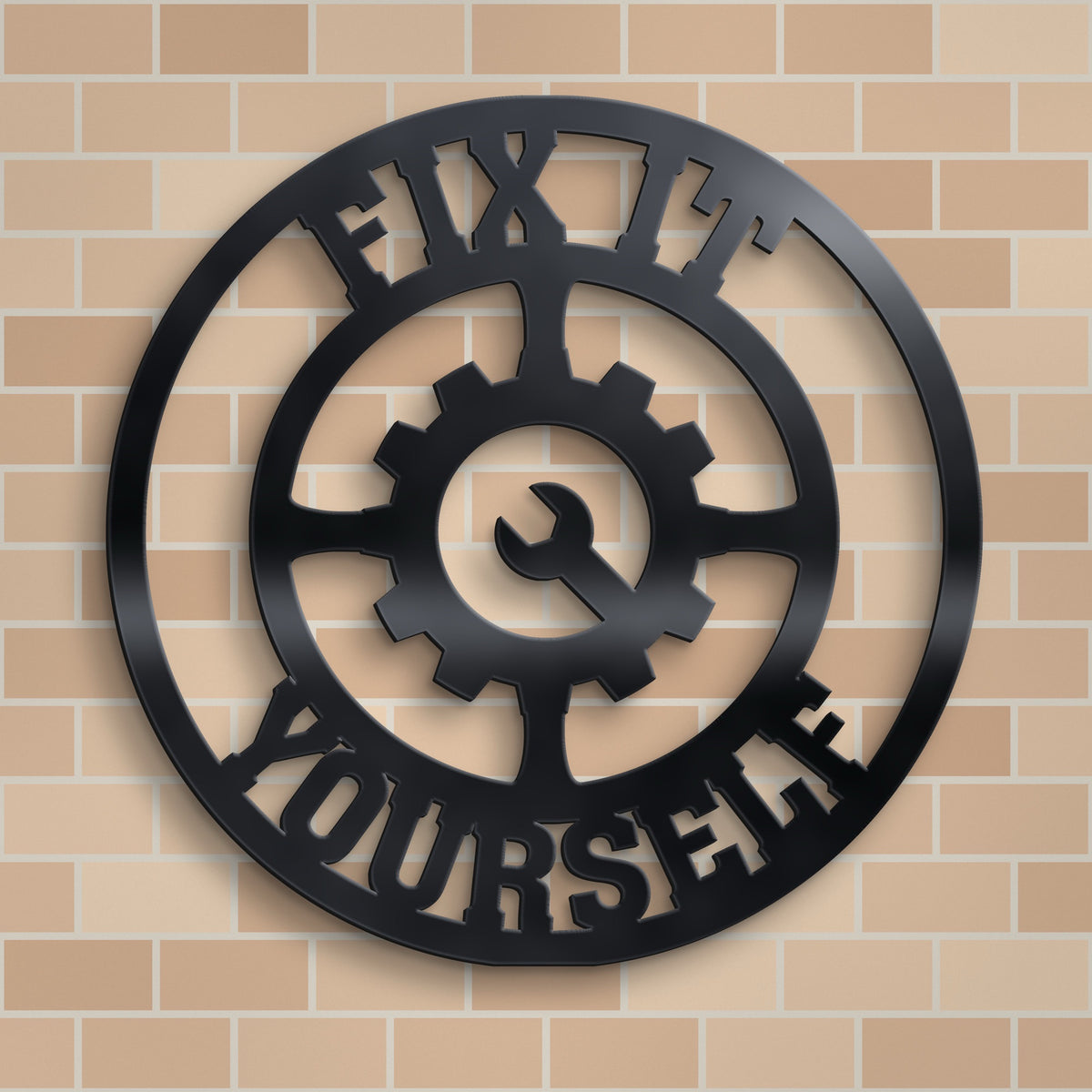 Black metal wall art featuring a circular design with a central gear and wrench motif, surrounded by the words 'FIX IT YOURSELF' in cutout lettering, displayed against a beige brick wall.