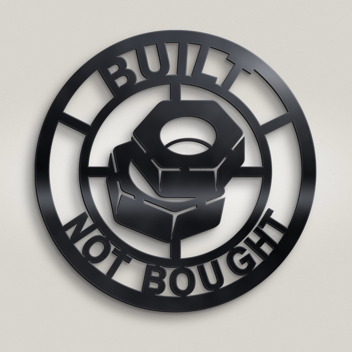 A circular black metal wall sign featuring a cutout design with a central nut motif and the words 'BUILT NOT BOUGHT' in bold lettering, shown against a light gray background.